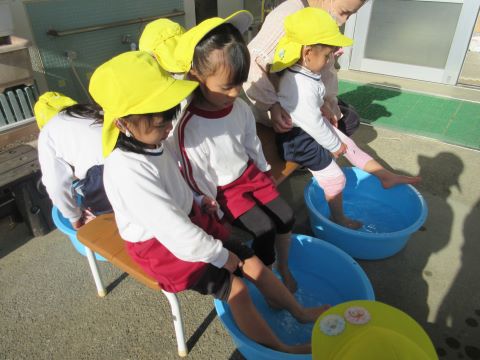 お湯の入ったたらいに足を入れて足湯を楽しむ園児